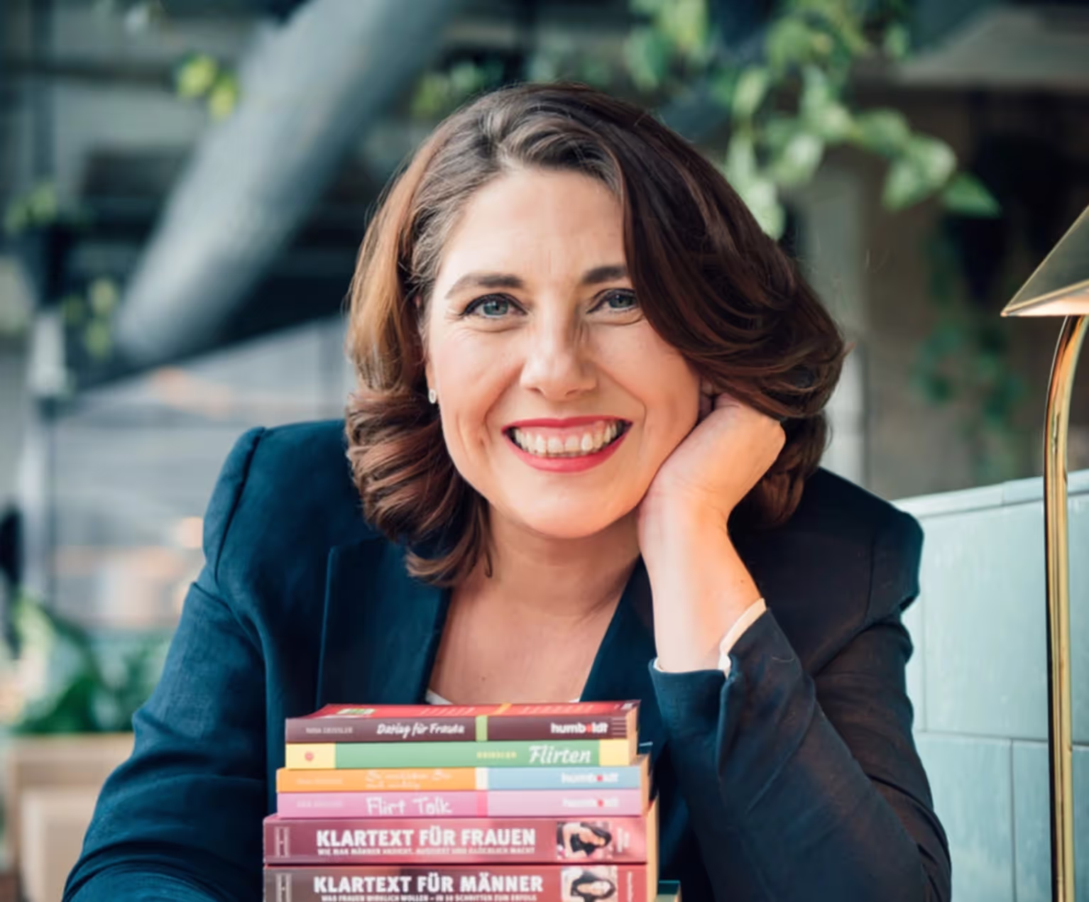 Foto einer blonden Frau mit mittellangen Haaren und einer rosa Bluse vor einem verschwommenen Hintergrund