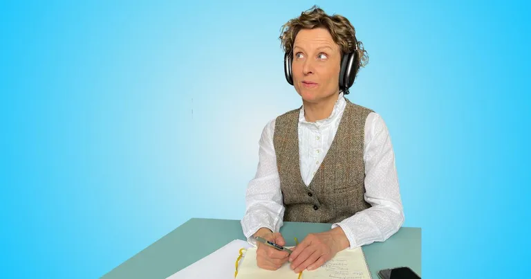 Ein Bild von Sandra Holze, auf dem sie Kopfhörer trägt und an einem Tisch sitzt.